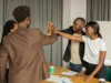 A group of diverse professionals high-fiving in an office setting, showcasing teamwork and collaboration.